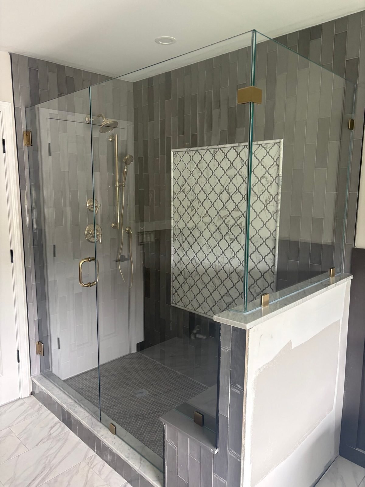 Glass shower enclosure with gray plank tile, patterned accent wall and brass hardware